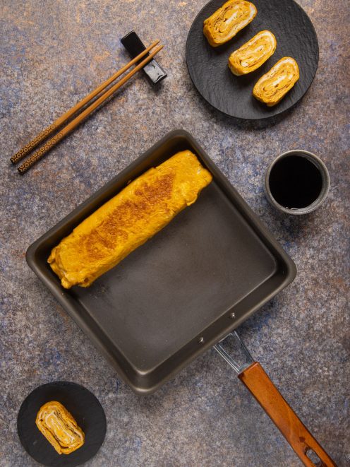 Tamagoyaki appena arrotolato nella padella rettangolare, con fette già tagliate che mostrano gli strati interni