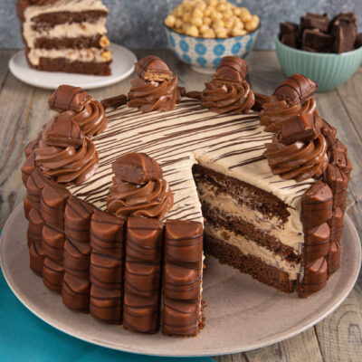 Torta Kinder Bueno a strati con crema alla nocciola, rivestita di cioccolatini e decorata con ciuffi di crema