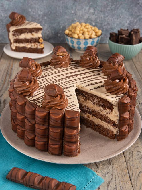 Torta Kinder Bueno a strati con crema alla nocciola, rivestita di cioccolatini e decorata con ciuffi di crema
