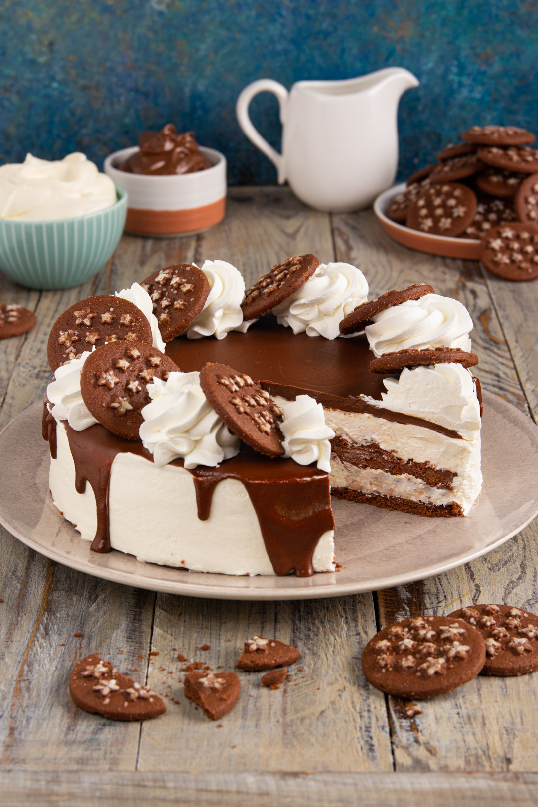 Torta Pan di Stelle con drip al cioccolato, ciuffi di panna e biscotti in superficie, con una fetta già tagliata