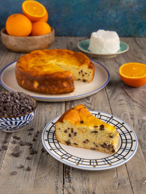 Torta ricotta e cioccolato tagliata a fette, con gocce di cioccolato e arance a fianco