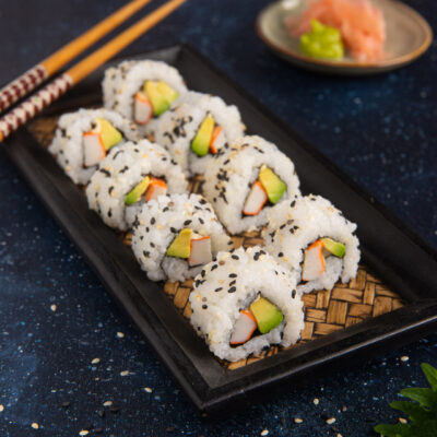 Uramaki al sesamo nero e bianco con surimi e avocado disposti in fila su vassoio