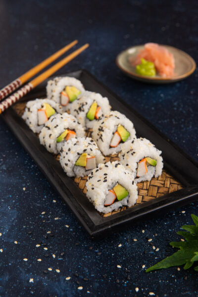 Uramaki al sesamo nero e bianco con surimi e avocado disposti in fila su vassoio