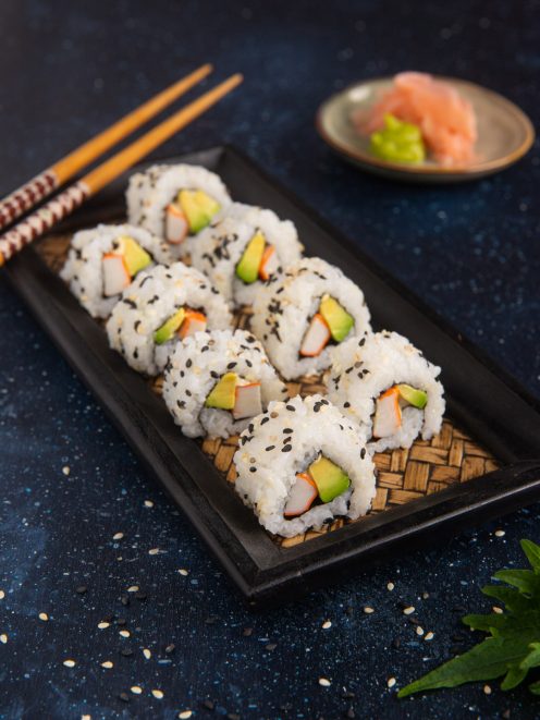 Uramaki al sesamo nero e bianco con surimi e avocado disposti in fila su vassoio