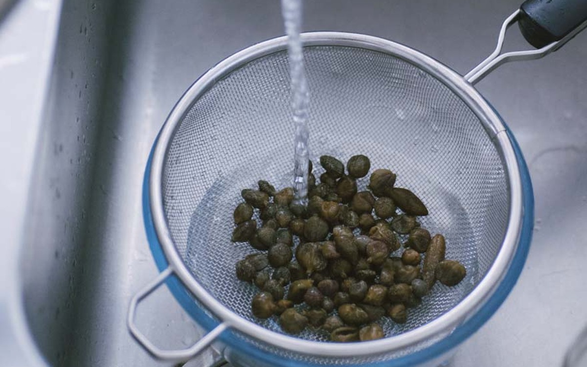 Capperi sciacquati sotto un getto d'acqua corrente in un colino a rete fine