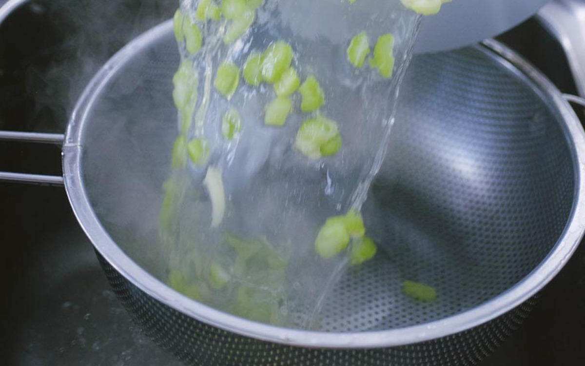 Sedano a tocchetti scolato in un colino mentre l'acqua bollente fuma