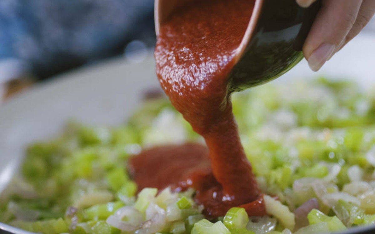 Passata di pomodoro versata su cipolla e sedano soffritti in padella