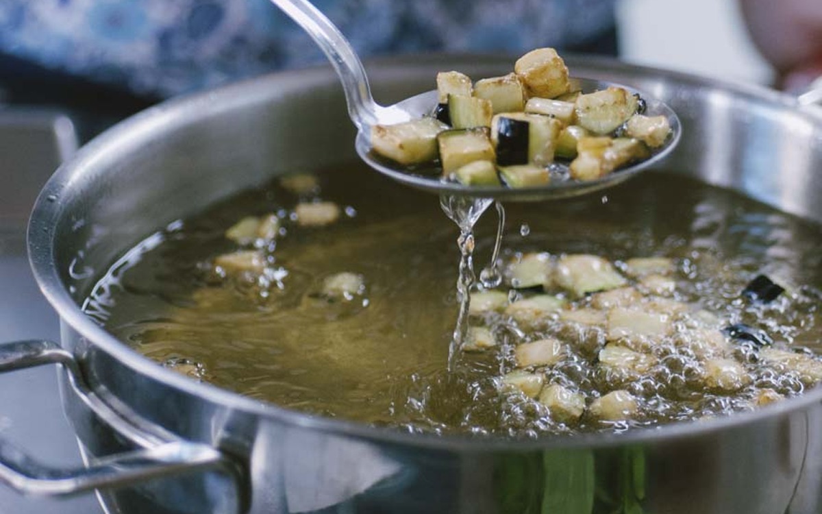 Dadini di melanzana dorati scolati con una schiumarola dall'olio bollente per la caponata