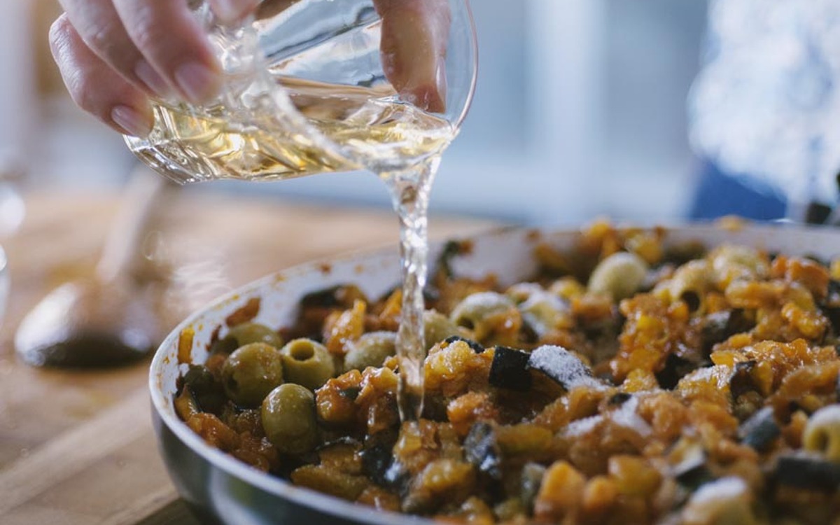Aceto versato in padella sulla caponata con melanzane, olive verdi e sedano