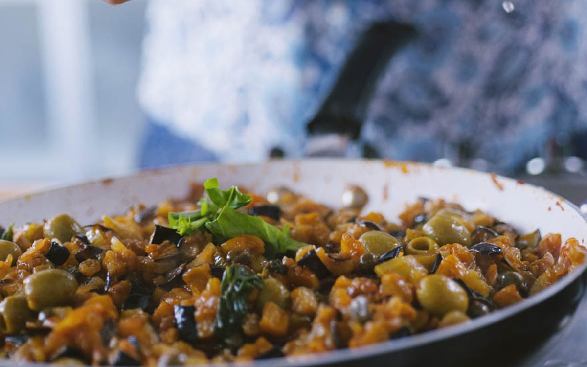 Melanzane, olive e sedano si insaporiscono in padella profumati da foglie di basilico fresco