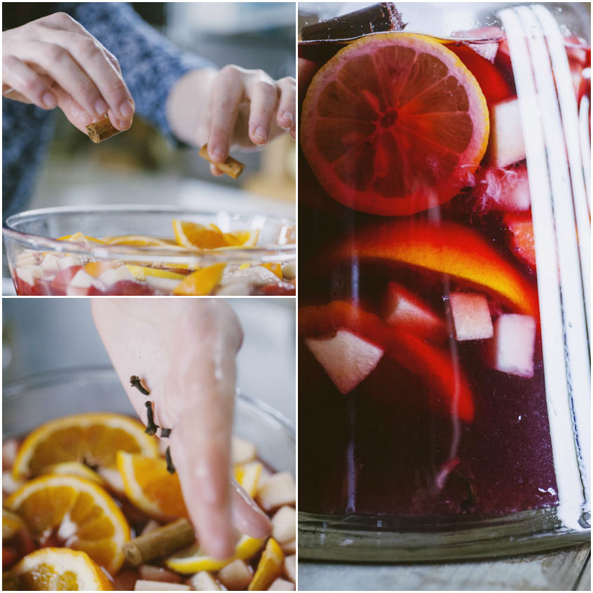 Mani che aggiungono cannella e chiodi di garofano alla sangria con fette di arancia e frutta