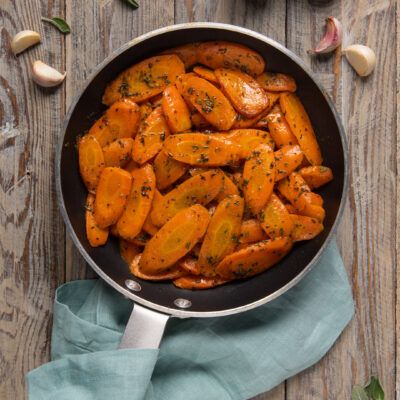 Carote in padella saltate con aglio ed erbe aromatiche tritate, lucide e ben caramellate
