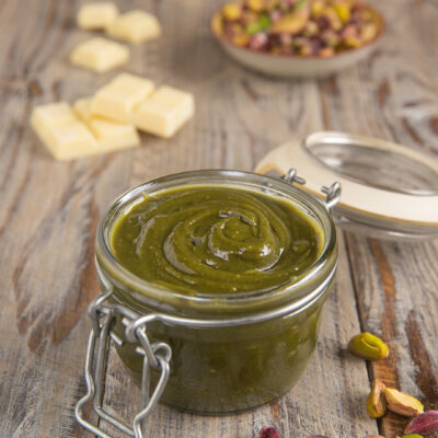 Crema di pistacchio in un vasetto di vetro con chiusura a scatto, circondata da pistacchi sgusciati