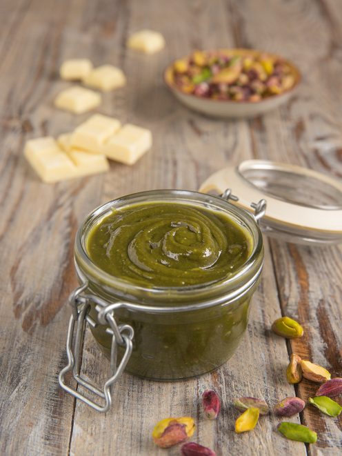 Crema di pistacchio in un vasetto di vetro con chiusura a scatto, circondata da pistacchi sgusciati