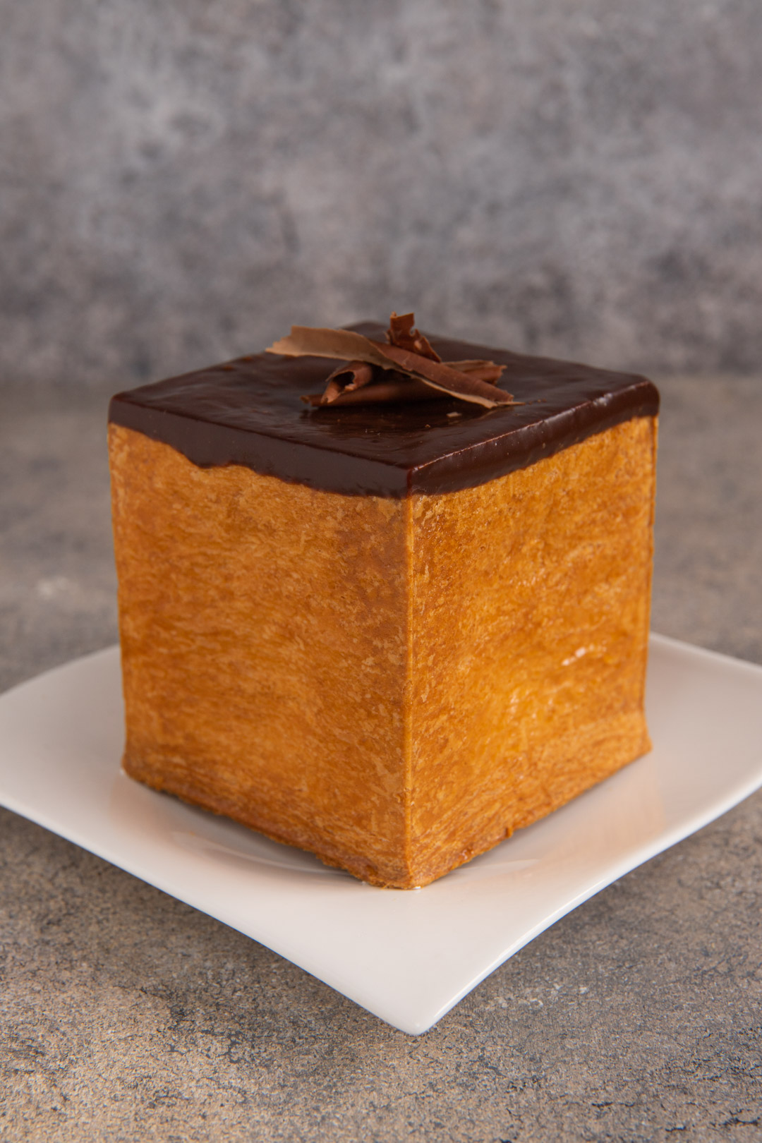 Cubo di pasta sfoglia glassato al cioccolato e decorato con riccioli di fondente in cima