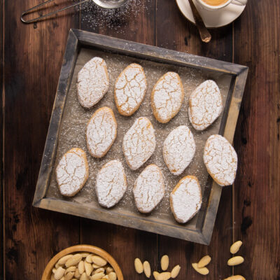 Ricciarelli disposti su teglia con zucchero a velo e mandorle pelate accanto
