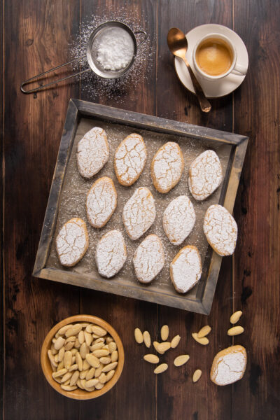 Ricciarelli disposti su teglia con zucchero a velo e mandorle pelate accanto
