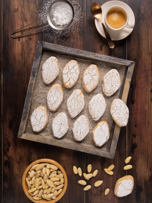 Ricciarelli disposti su teglia con zucchero a velo e mandorle pelate accanto