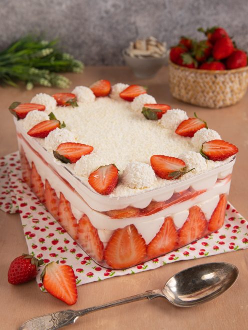 Tiramisù al cocco e fragole a strati con panna, fragole fresche a fette e palline al cocco in superficie