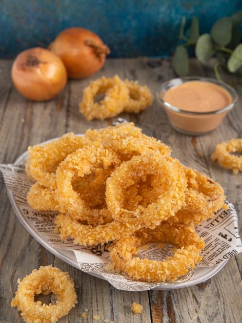 Anelli di cipolla fritti con panatura croccante, serviti con salsa rosa a parte
