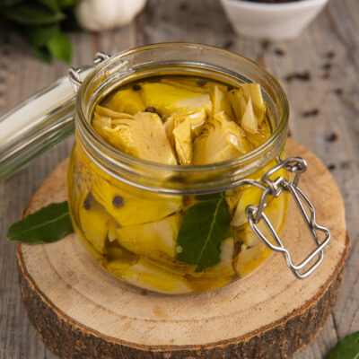 Carciofini sott'olio in vasetto con foglie di alloro e grani di pepe