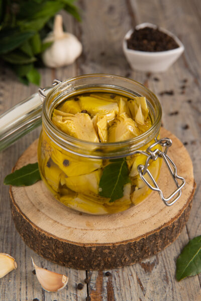 Carciofini sott'olio in vasetto con foglie di alloro e grani di pepe