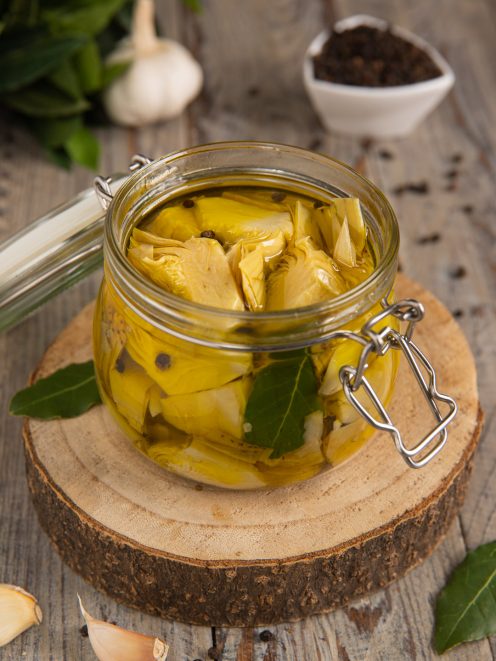 Carciofini sott'olio in vasetto con foglie di alloro e grani di pepe