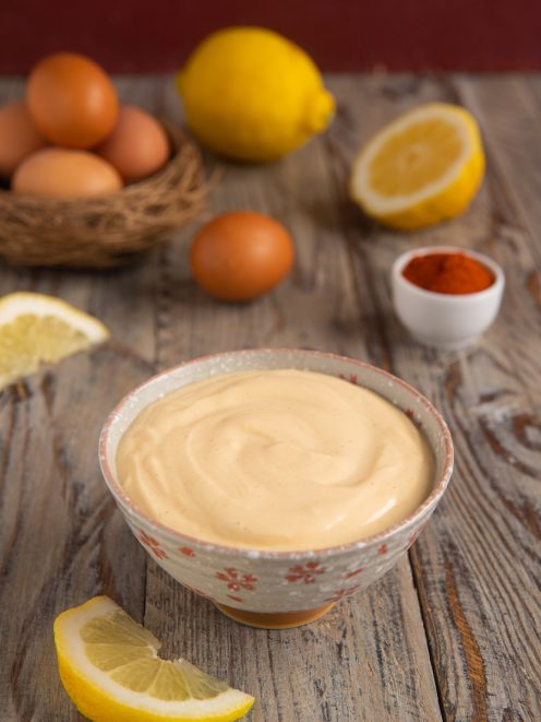 Maionese vellutata in ciotola con uova, limoni e paprika dolce sul tavolo di legno