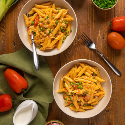 Penne ai 7 peccati con piselli, pancetta e pomodoro in due ciotole servite sul tavolo