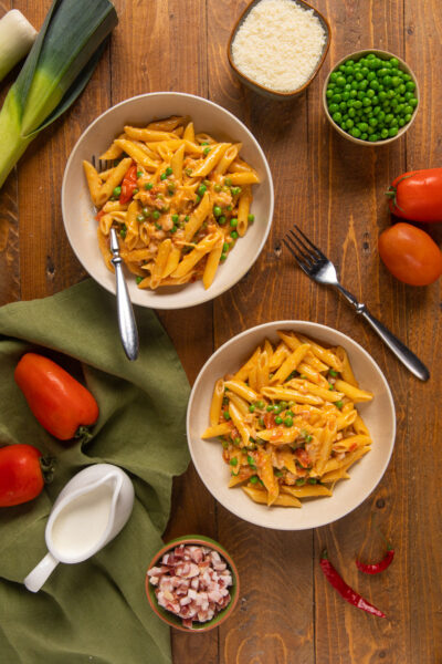 Penne ai 7 peccati con piselli, pancetta e pomodoro in due ciotole servite sul tavolo