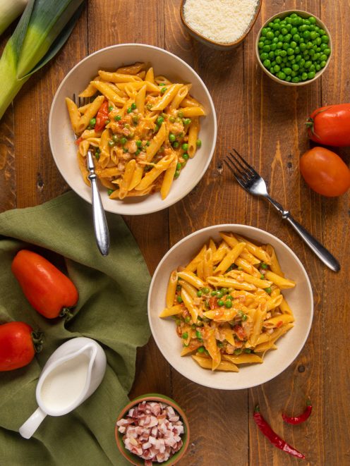 Penne ai 7 peccati con piselli, pancetta e pomodoro in due ciotole servite sul tavolo