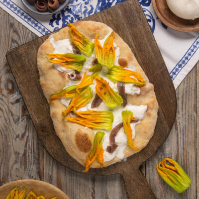 Pinsa con alici, fiori di zucca e burrata appena sfornata su tagliere in legno