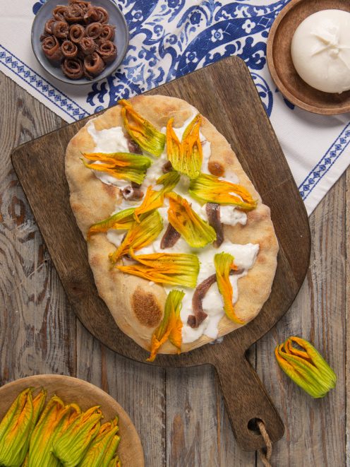 Pinsa con alici, fiori di zucca e burrata appena sfornata su tagliere in legno