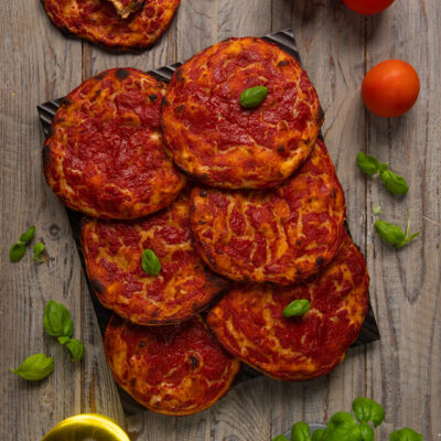 Pizzette rosse croccanti con sugo di pomodoro e foglie di basilico fresco