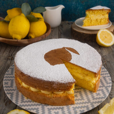 Torta con crema al limone spolverata di zucchero a velo, con una fetta tagliata che mostra il ripieno cremoso