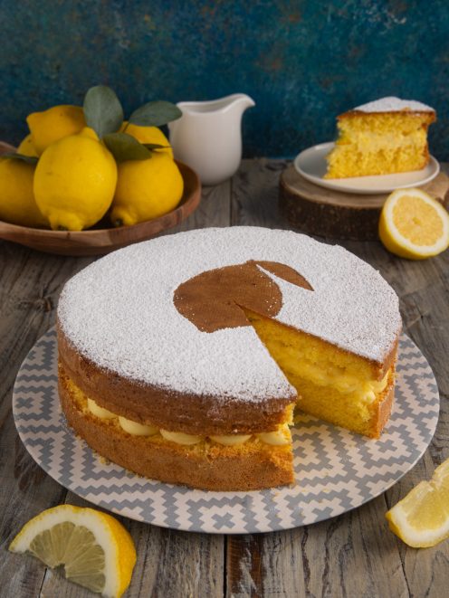 Torta con crema al limone spolverata di zucchero a velo, con una fetta tagliata che mostra il ripieno cremoso