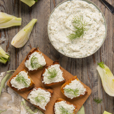 Tzatziki di finocchi in ciotola e spalmato su crostini di pane, guarnito con ciuffi di finocchio