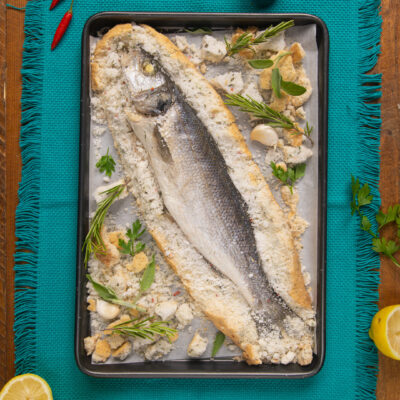 Branzino al sale appena sfornato con la crosta rotta, rosmarino e aglio attorno