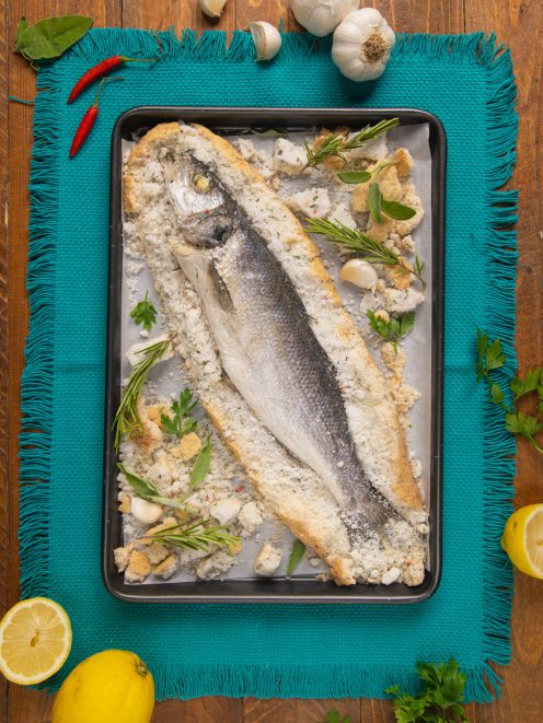 Branzino al sale appena sfornato con la crosta rotta, rosmarino e aglio attorno