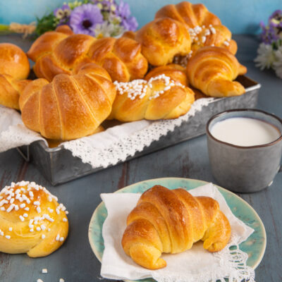 Brioche soffici appena sfornate, alcune a cornetto e altre a girella con granella di zucchero