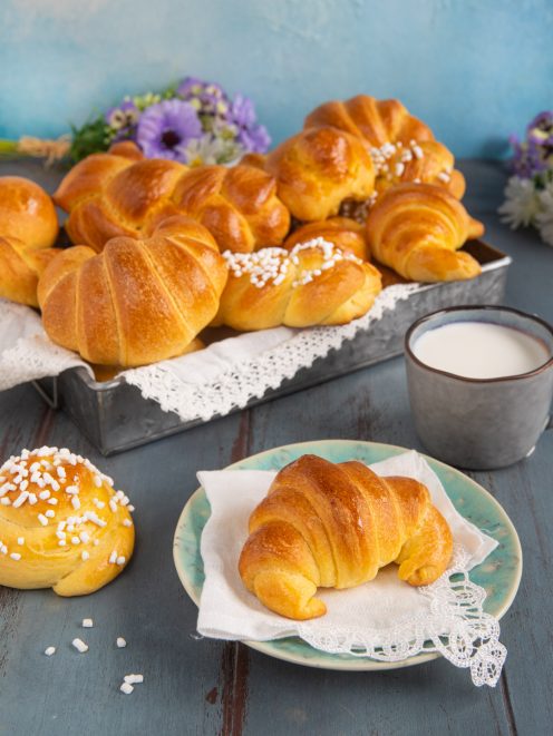 Brioche soffici appena sfornate, alcune a cornetto e altre a girella con granella di zucchero