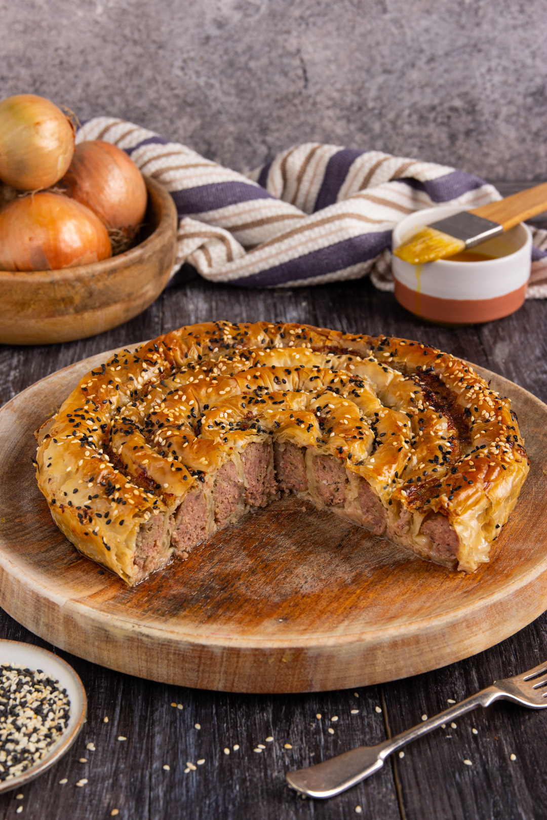 Burek a spirale appena sfornato, con pasta sfoglia dorata e semi di sesamo, tagliato a mostrare il ripieno di carne