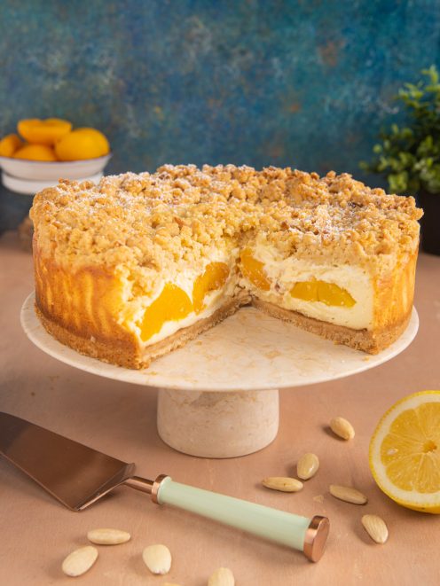 Cheesecake alle pesche con crumble, farcita di crema e pesche a fette, tagliata a metà