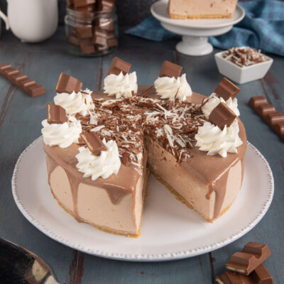 Kinder cheesecake affettata con glassa al cioccolato colante, ciuffi di panna e scaglie di cioccolato
