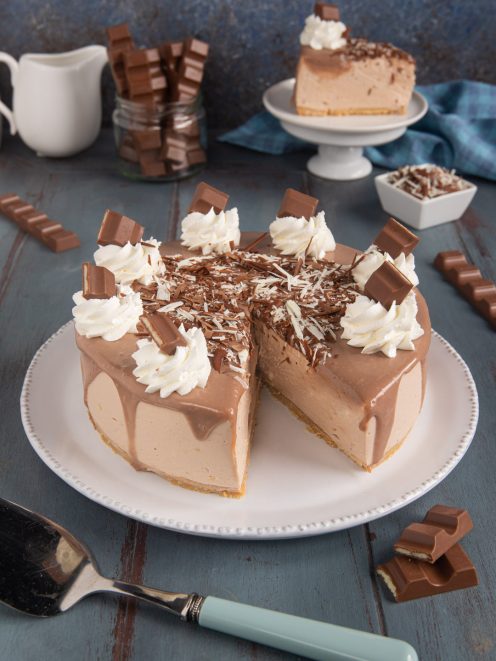 Kinder cheesecake affettata con glassa al cioccolato colante, ciuffi di panna e scaglie di cioccolato