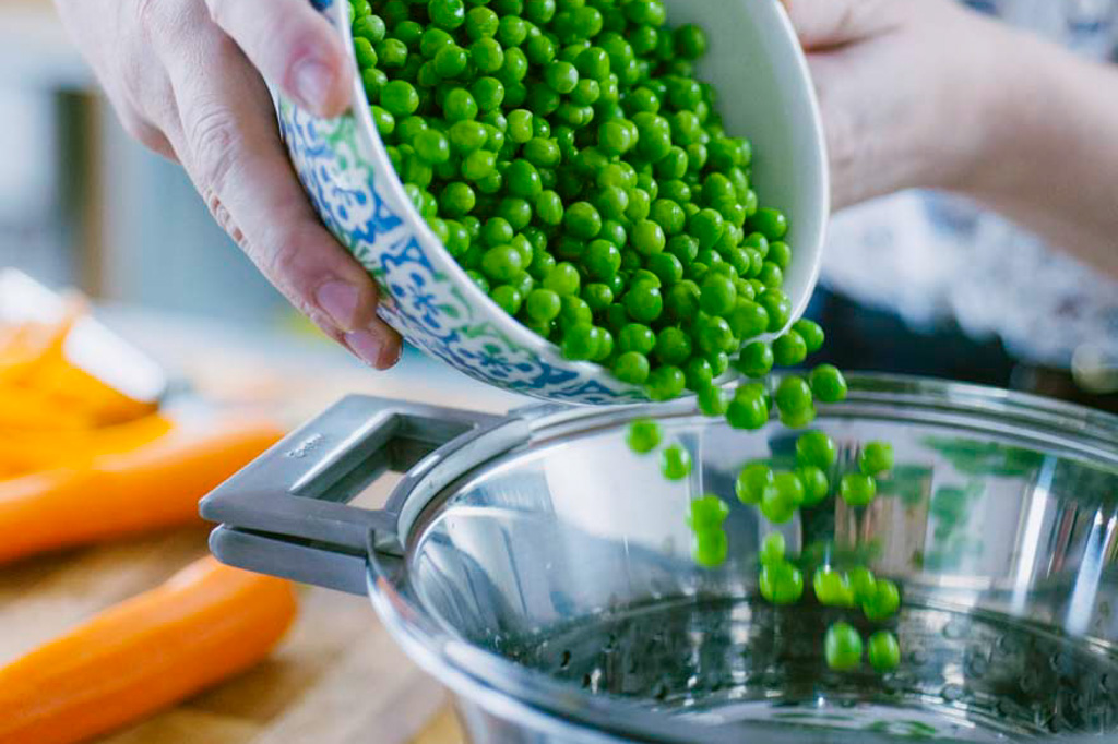 Piselli freschi versati in uno scolapasta con acqua bollente