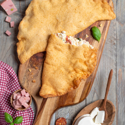 Pizza fritta dorata su tagliere, con ripieno di ricotta e salumi in bella vista