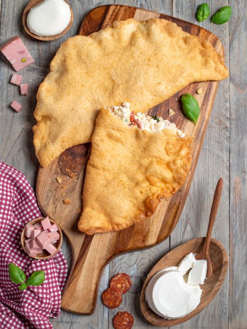 Pizza fritta dorata su tagliere, con ripieno di ricotta e salumi in bella vista