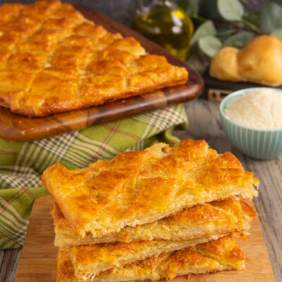 Fette di pizza sfogliata dorata e croccante impilate su tagliere di legno