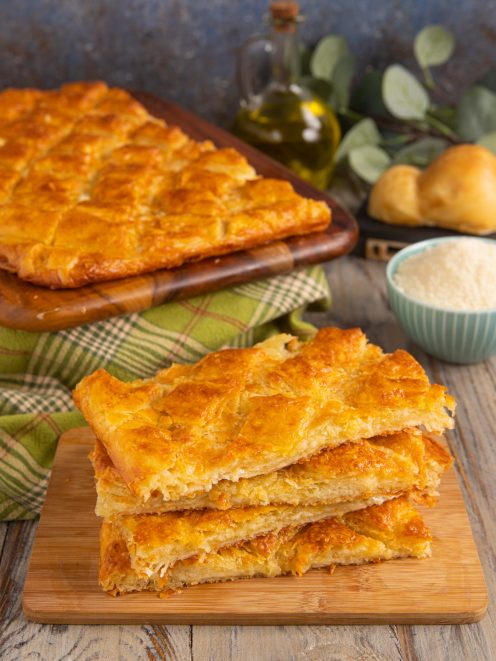 Fette di pizza sfogliata dorata e croccante impilate su tagliere di legno